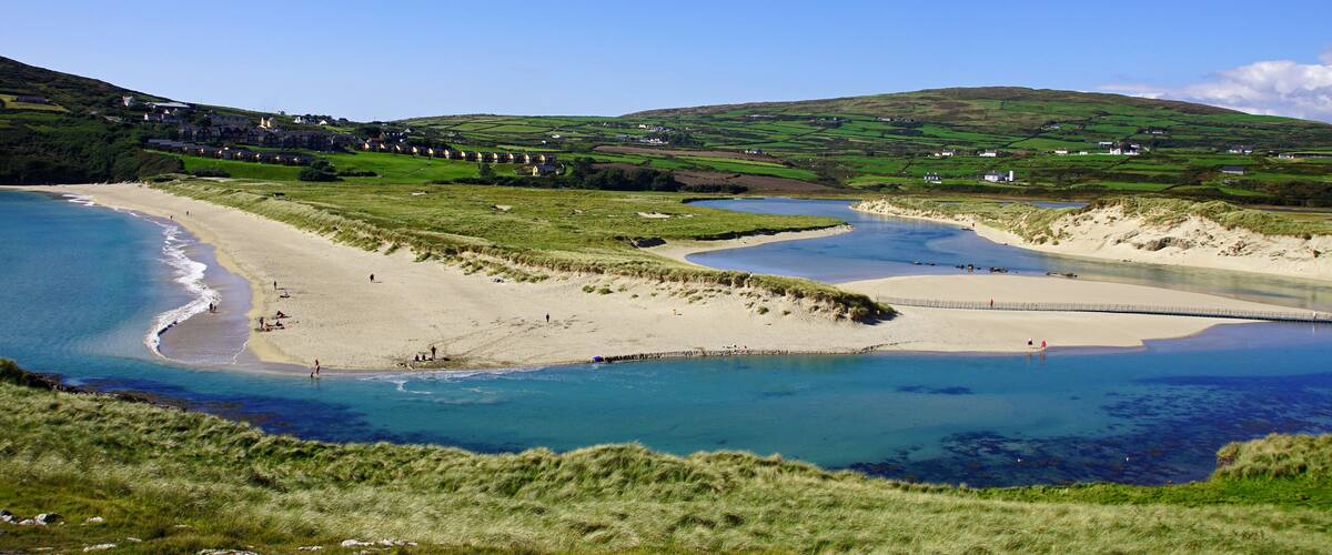 A coastal landscape with a beach, a river, and rolling hills.