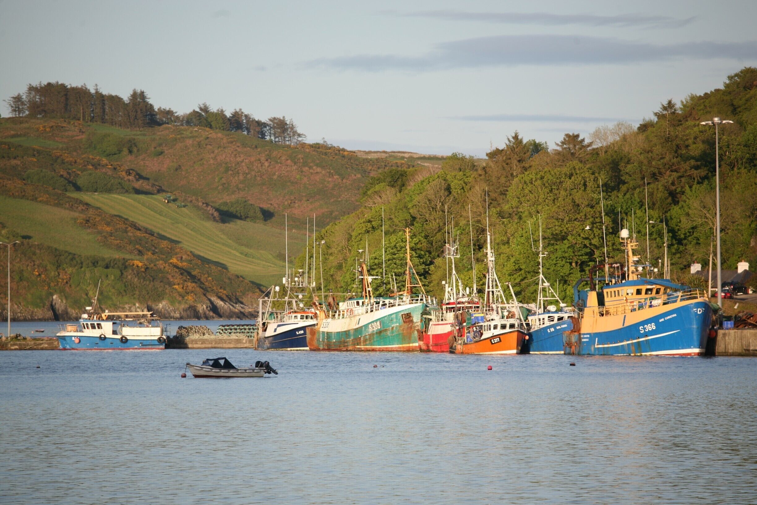 A harbor with several boats docked, surrounded by hills and trees.