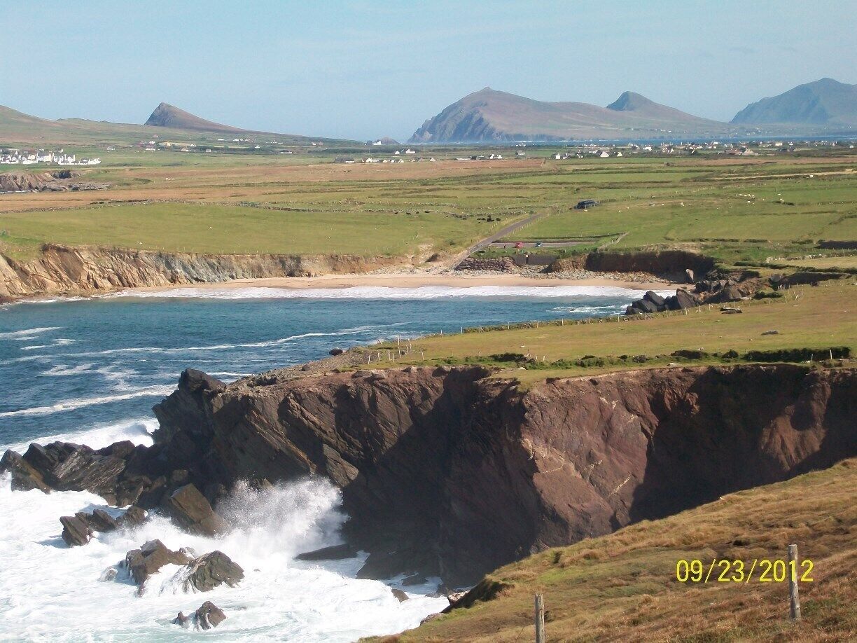 A coastal landscape with rocky cliffs, a sandy beach, and distant mountains.