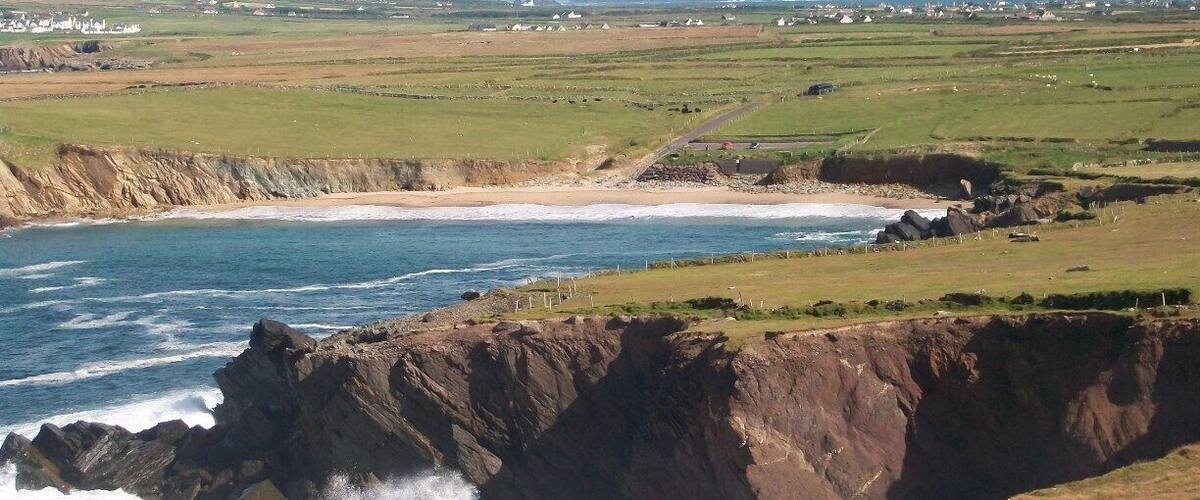 A coastal landscape with rocky cliffs, a sandy beach, and distant mountains.
