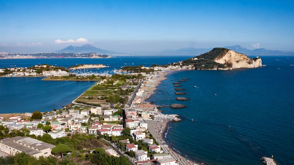 A coastal town with a beach, boats, and a mountain in the background.