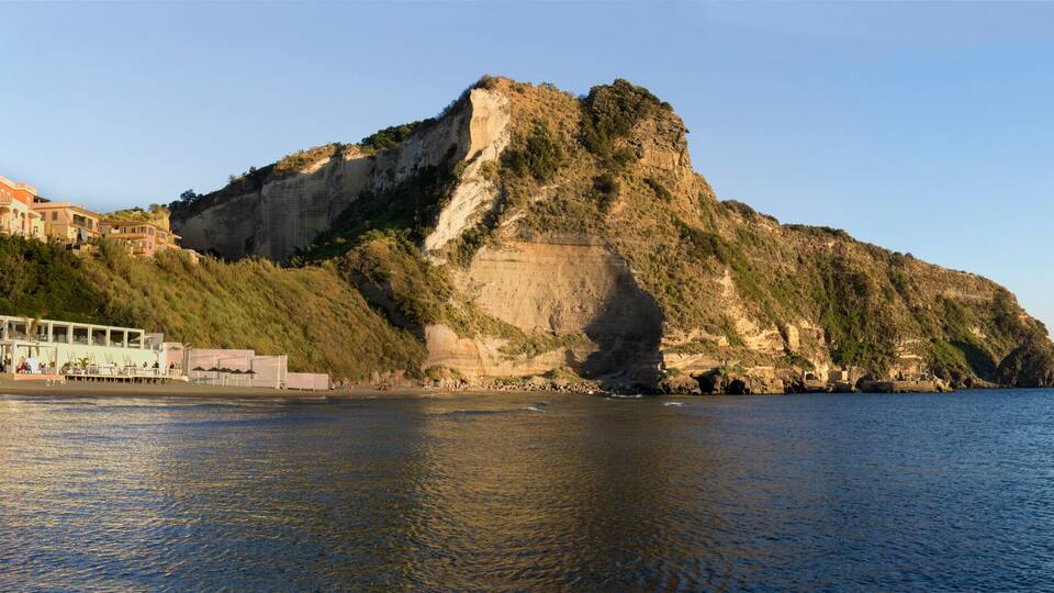 A coastal town with buildings along the shore, a prominent rocky cliff, and a calm sea.
