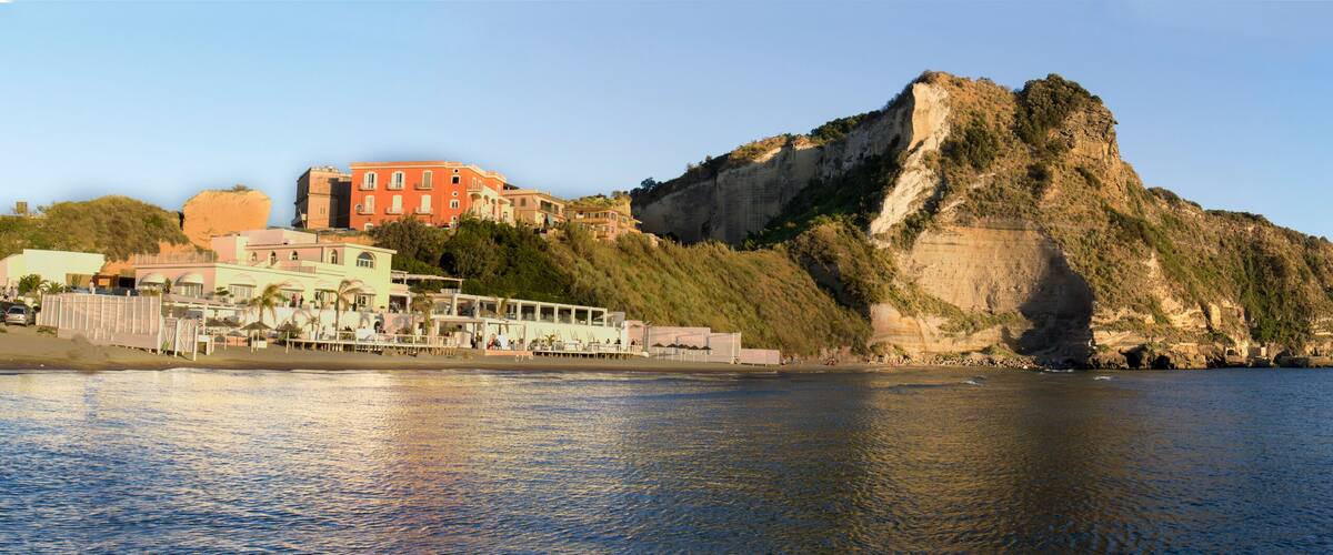A coastal town with buildings along the shore, a prominent rocky cliff, and a calm sea.