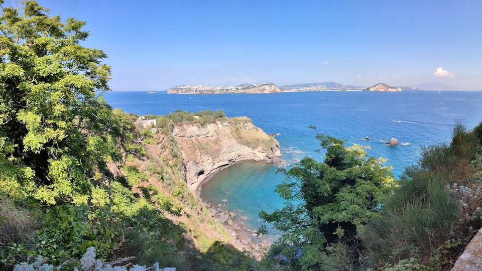 A coastal landscape with cliffs, a clear blue sea, and distant islands.