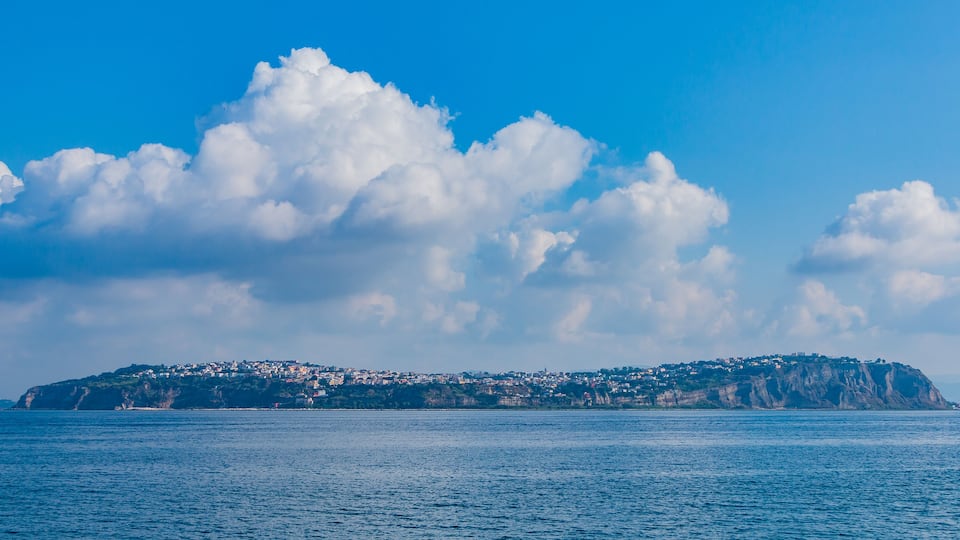 A coastal town with a prominent hill, a clear blue sky, and calm sea.