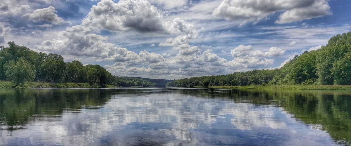 A calm river with dense forests on both sides and a cloudy sky.