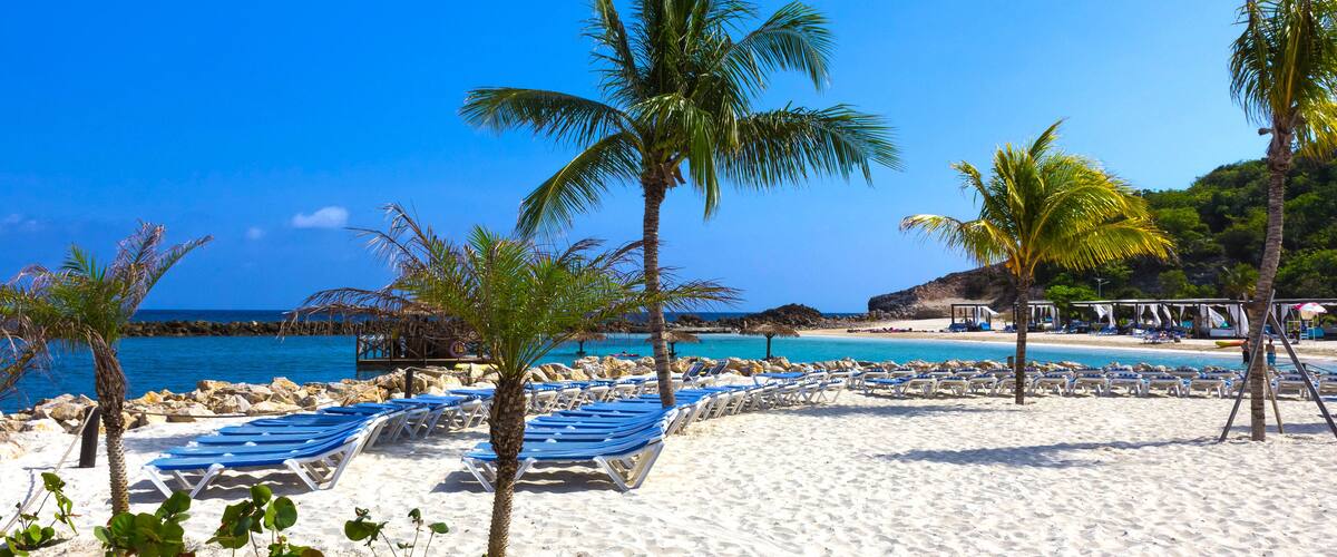 A beach with white sand, palm trees, and a clear blue sky.