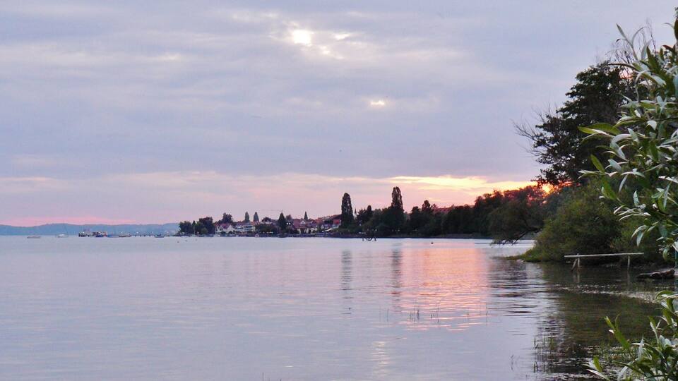 A calm lake with a row of houses and trees along the shore.