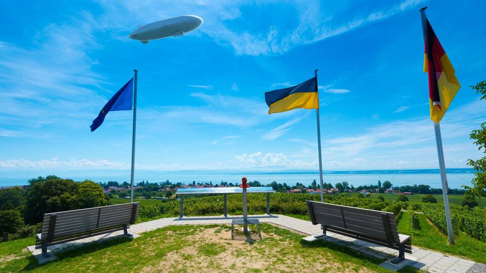 A park with benches, flags, and a distant view of a lake and buildings.