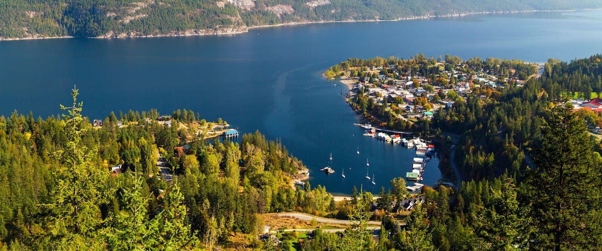 Une ville côtière nichée entre des montagnes, avec un lac paisible et des voiliers amarrés le long de la rive.
