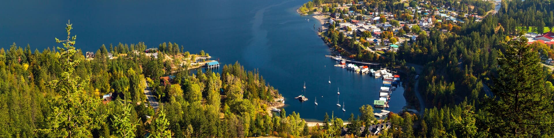 A coastal town nestled between mountains, with a calm lake and sailboats docked along the shore.