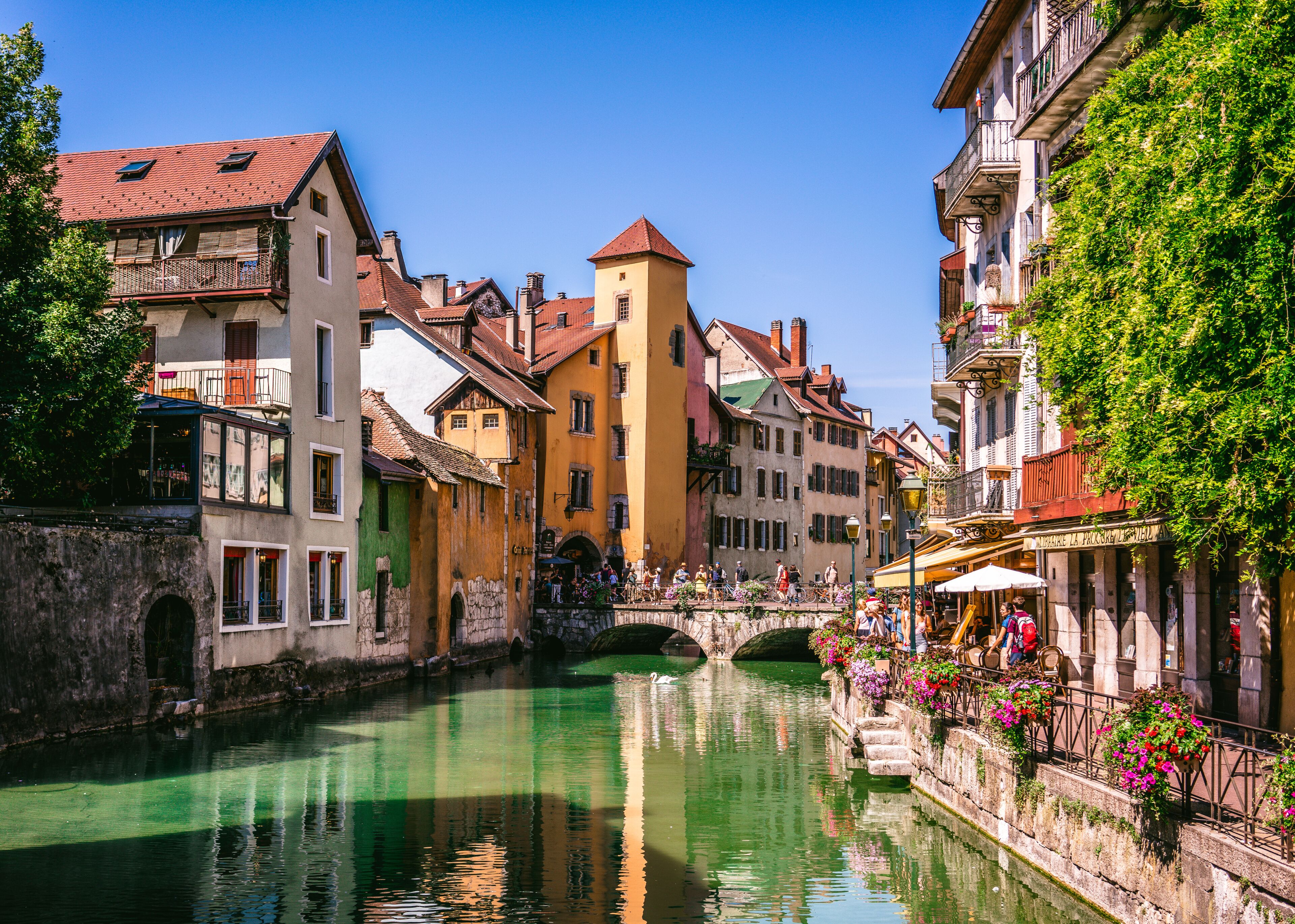 A canal with buildings on either side, a stone bridge, and a row of flower-adorned railings.
