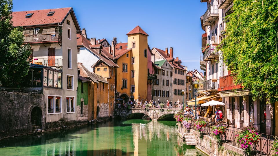 A canal with buildings on either side, a stone bridge, and a row of flower-adorned railings.