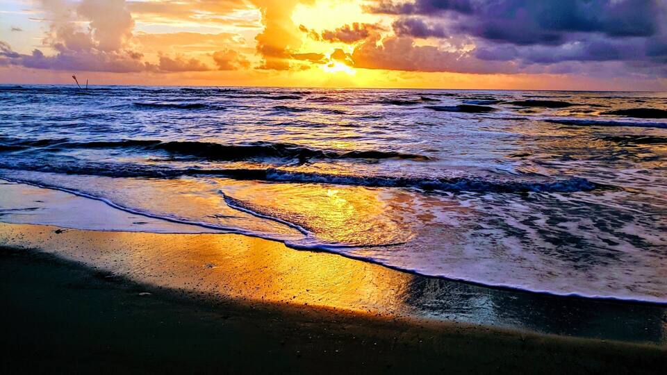 A sunset over the ocean with waves on the shore.