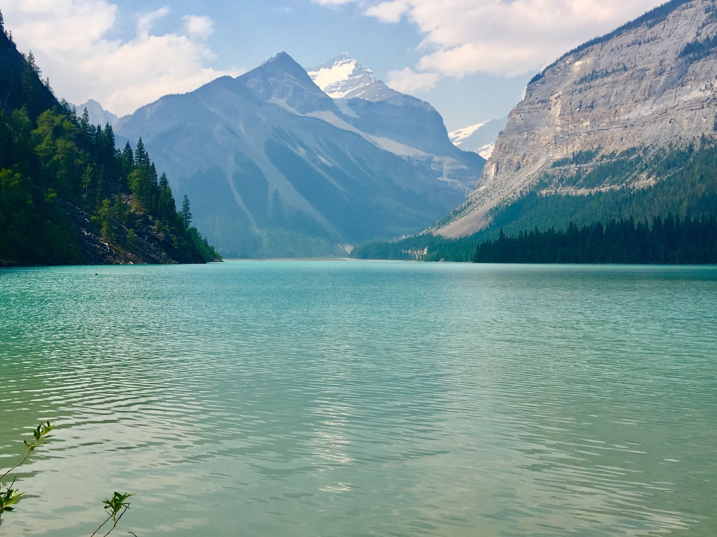 A calm lake surrounded by mountains with snow-capped peaks and dense forests.