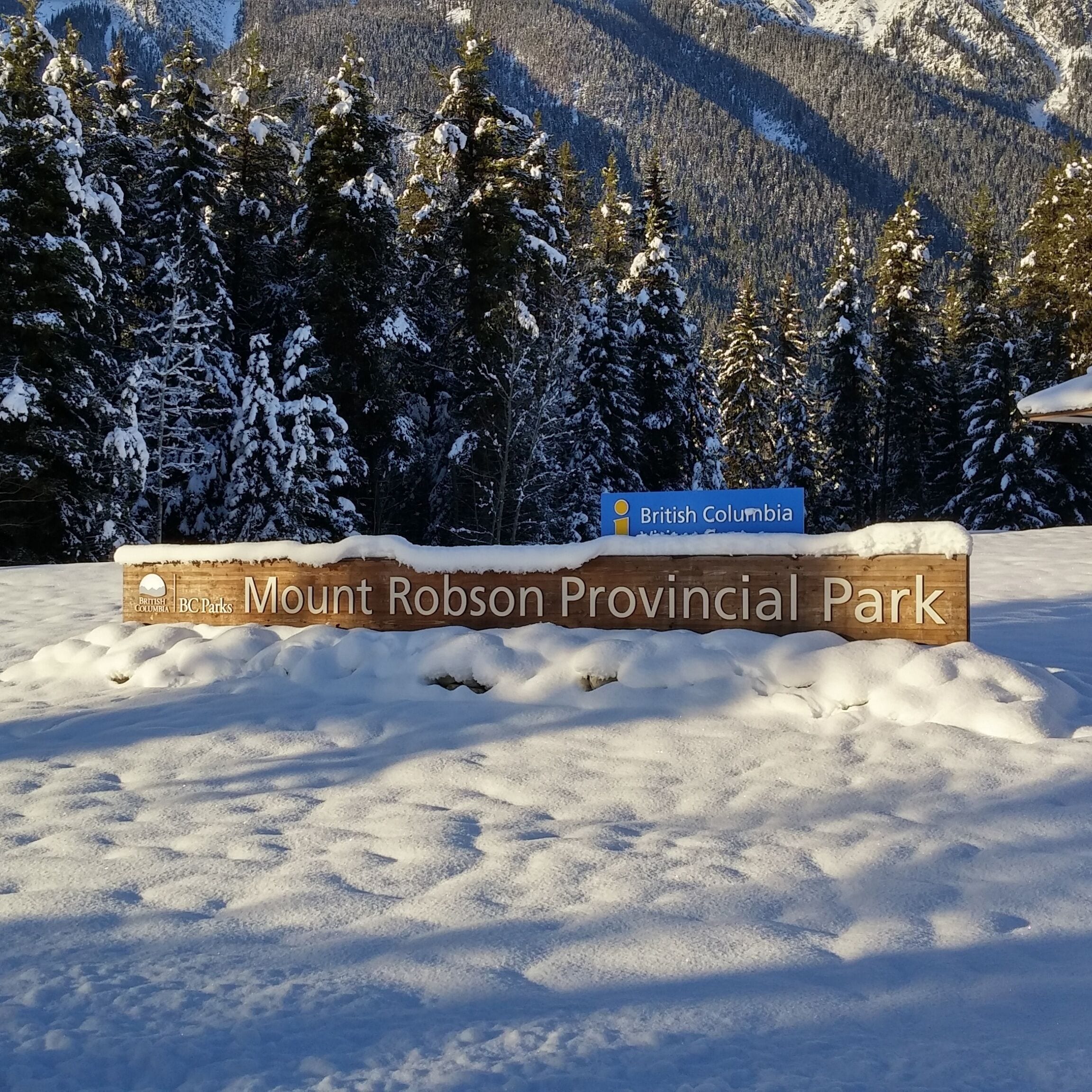 A sign for Mount Robson Provincial Park with snow-covered trees and mountains in the background.