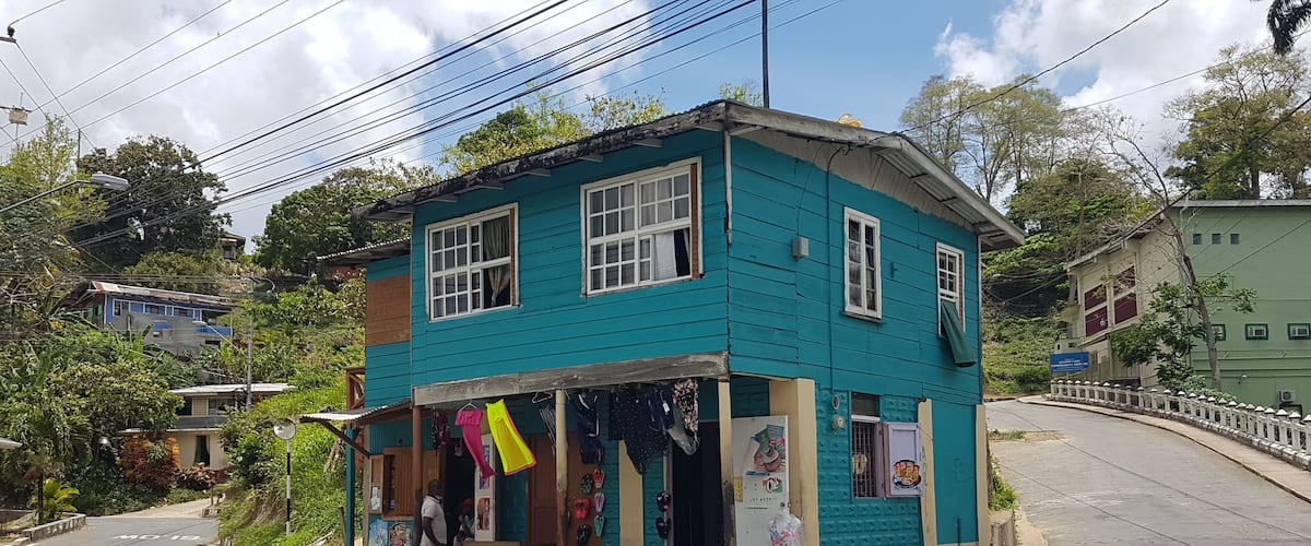 A turquoise building with a shop on the ground floor, a street with a yellow line, and a white fence along the road.