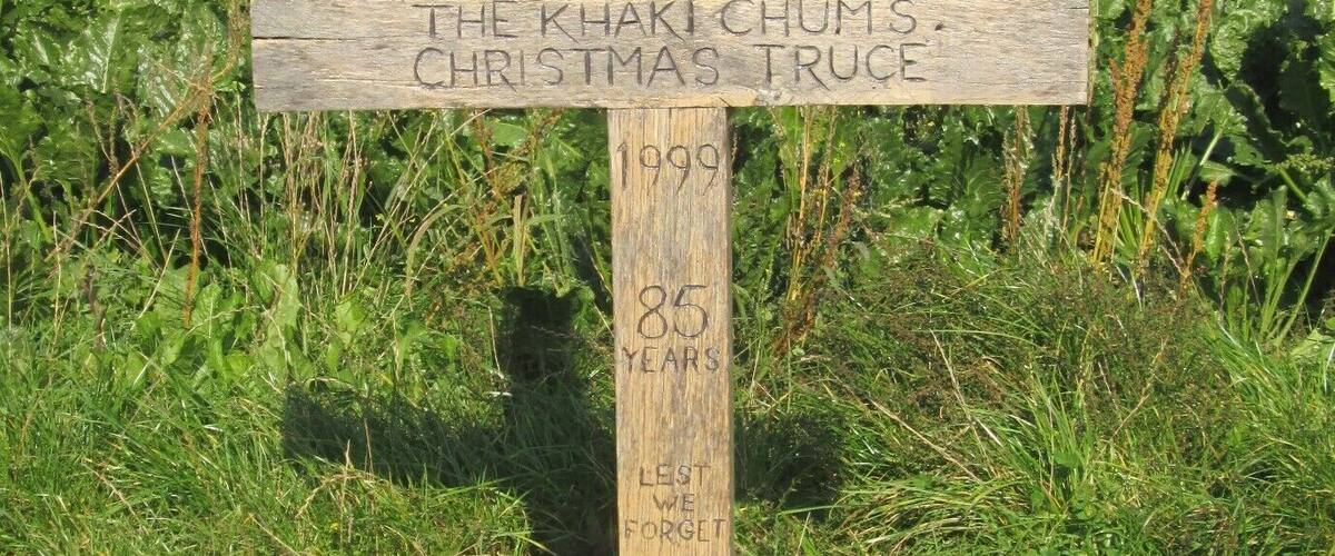 A wooden cross with inscriptions and a poppy wreath at its base.