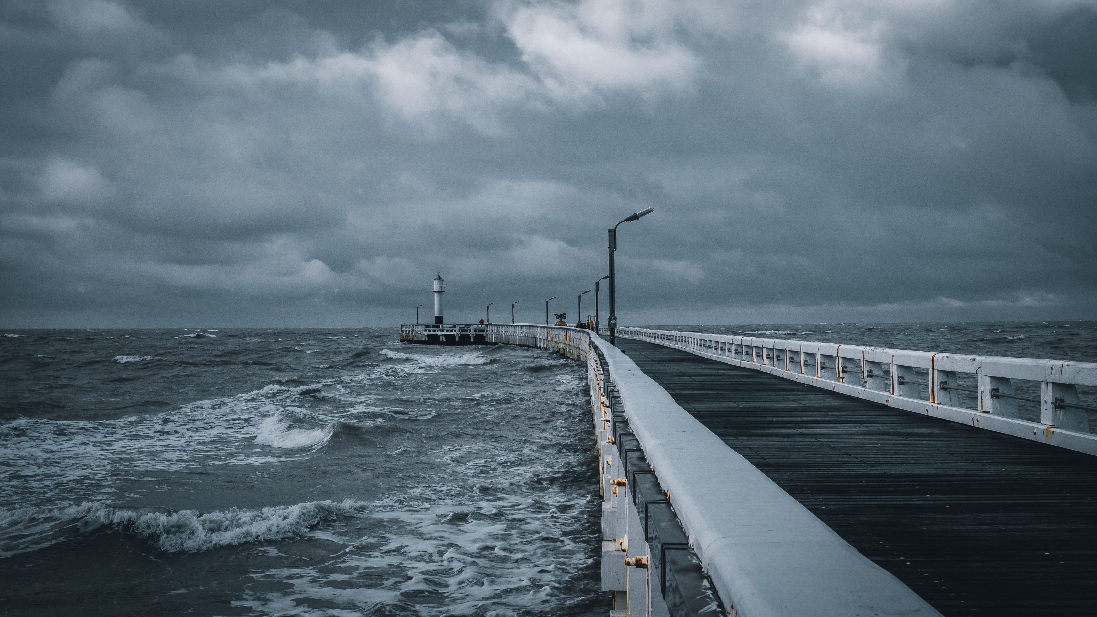 A pier extending into a stormy sea with a lighthouse in the distance.