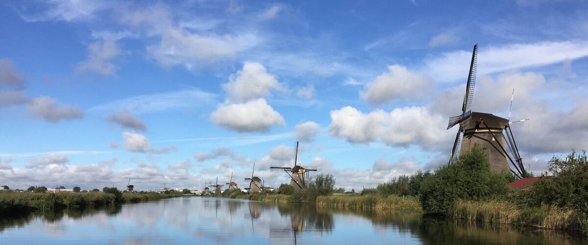 A calm river reflecting windmills and a modern tower.