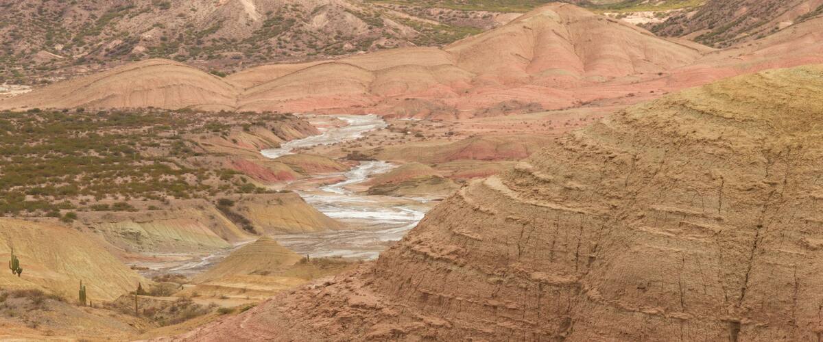 A rugged landscape with a river winding through a valley of colorful rock formations.