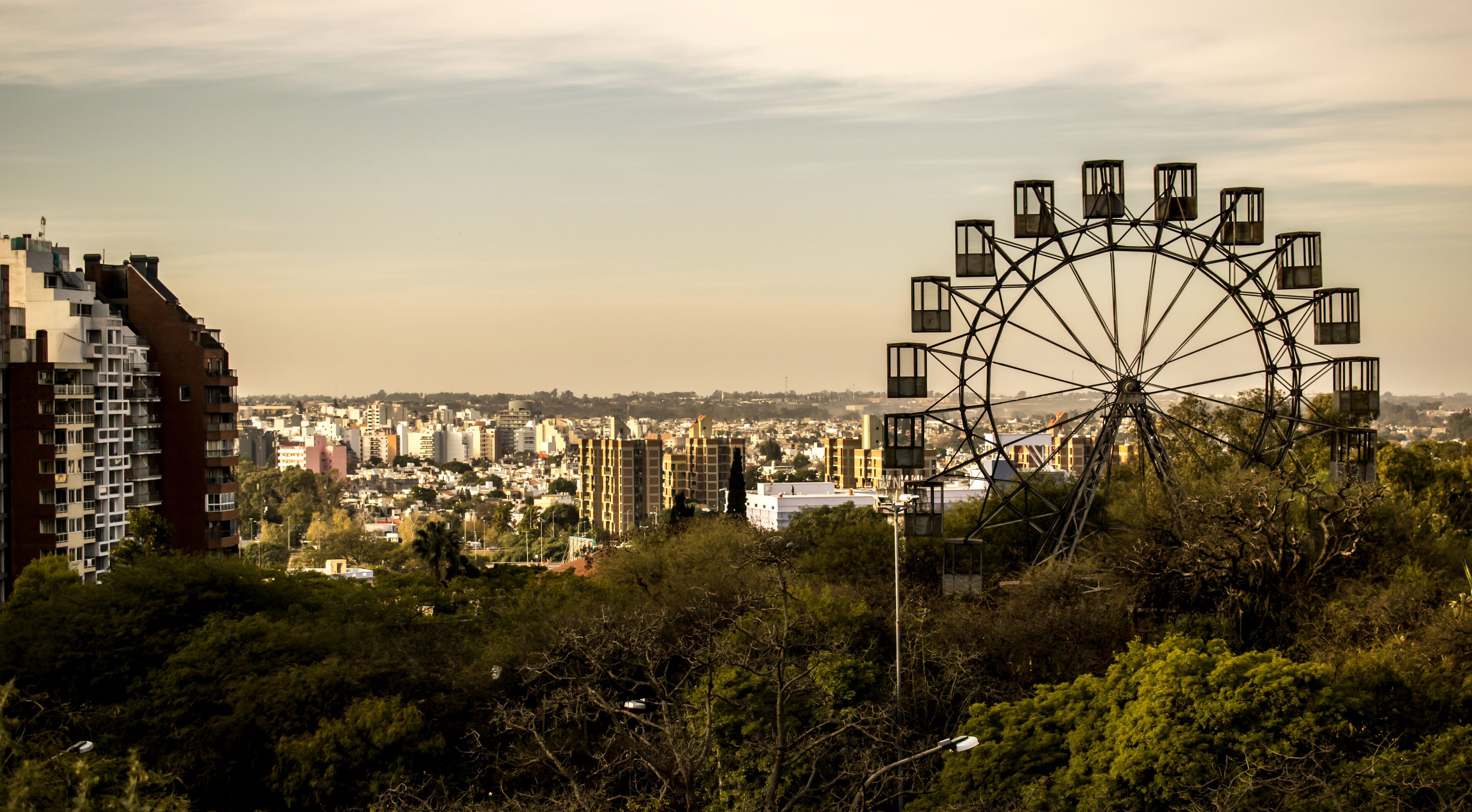 A Ferris wheel in a cityscape with buildings and trees.