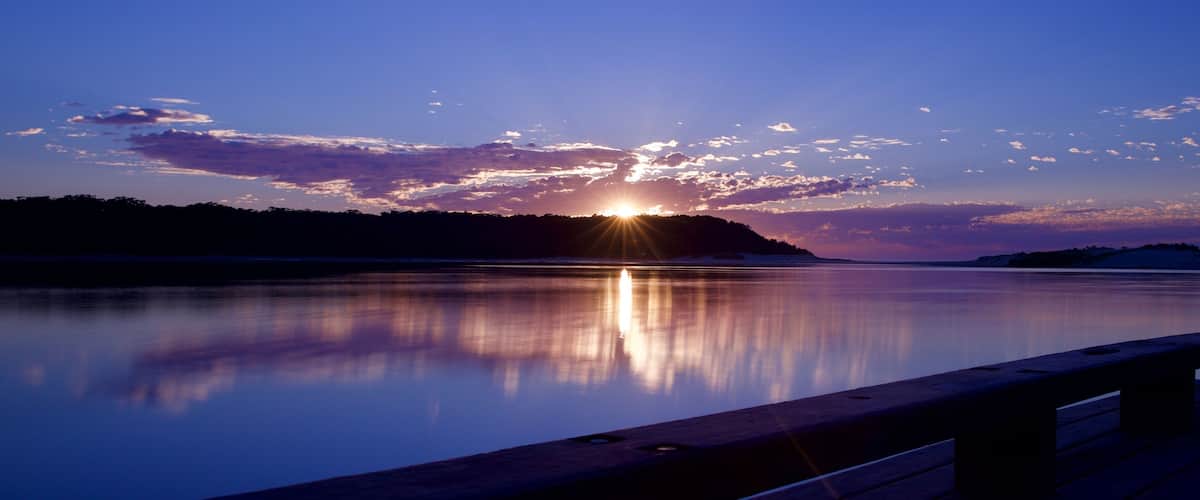 A sunset over a calm lake with a wooden dock.