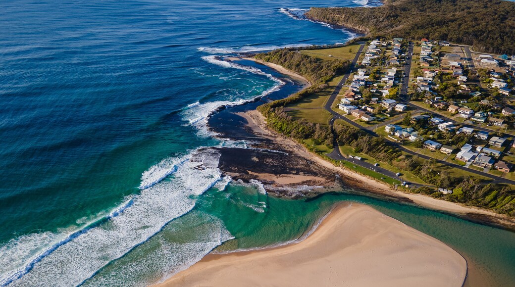 An aerial view of a coastal area with a beach, clear blue waters, and a residential neighborhood.