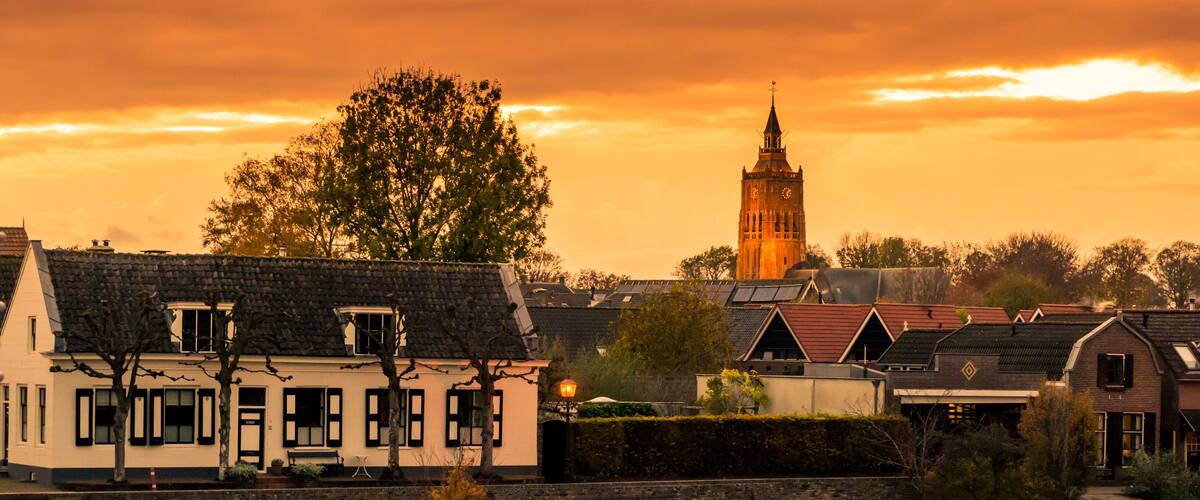 A town with traditional architecture, a prominent clock tower, and a sunset sky.