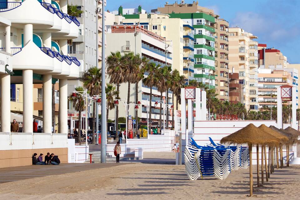 Une promenade en bord de mer, avec un hôtel, des palmiers et des parasols de plage.