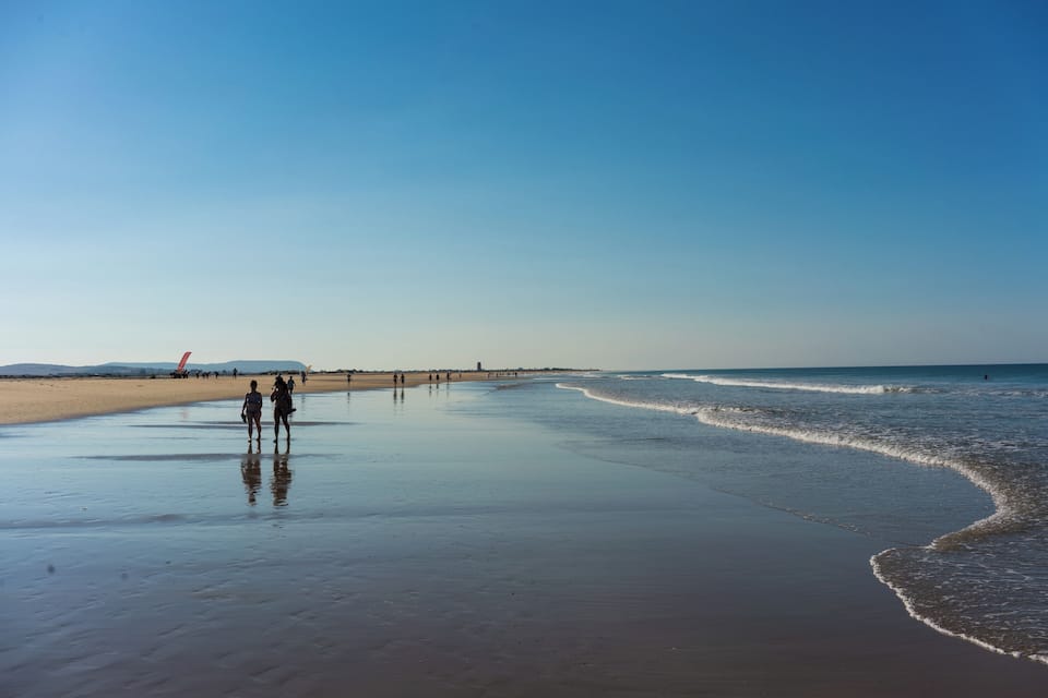 A wide beach with gentle waves, a clear sky, and distant mountains.