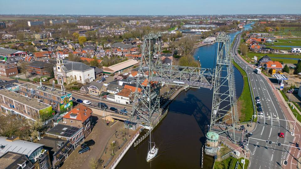 A river with a bridge, a boat, and a cityscape with buildings and roads.