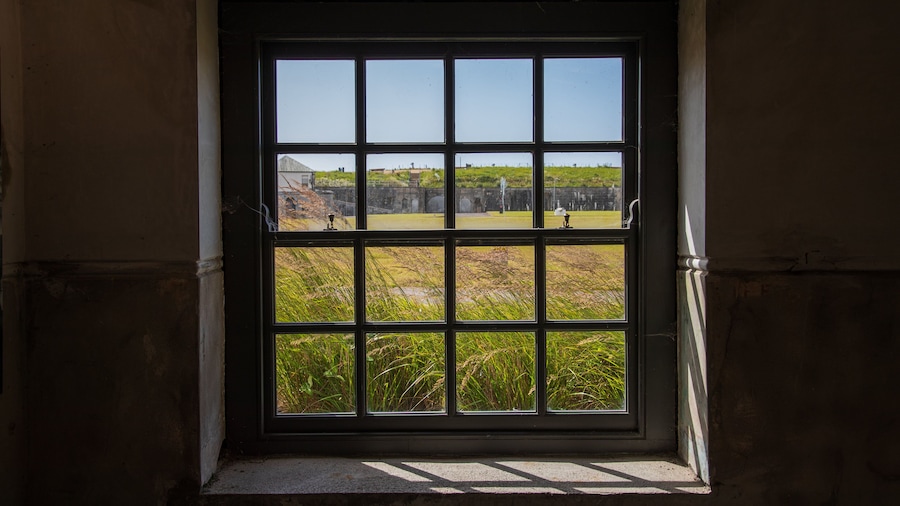 Una ventana con vista a un campo cubierto de hierba y un edificio lejano.