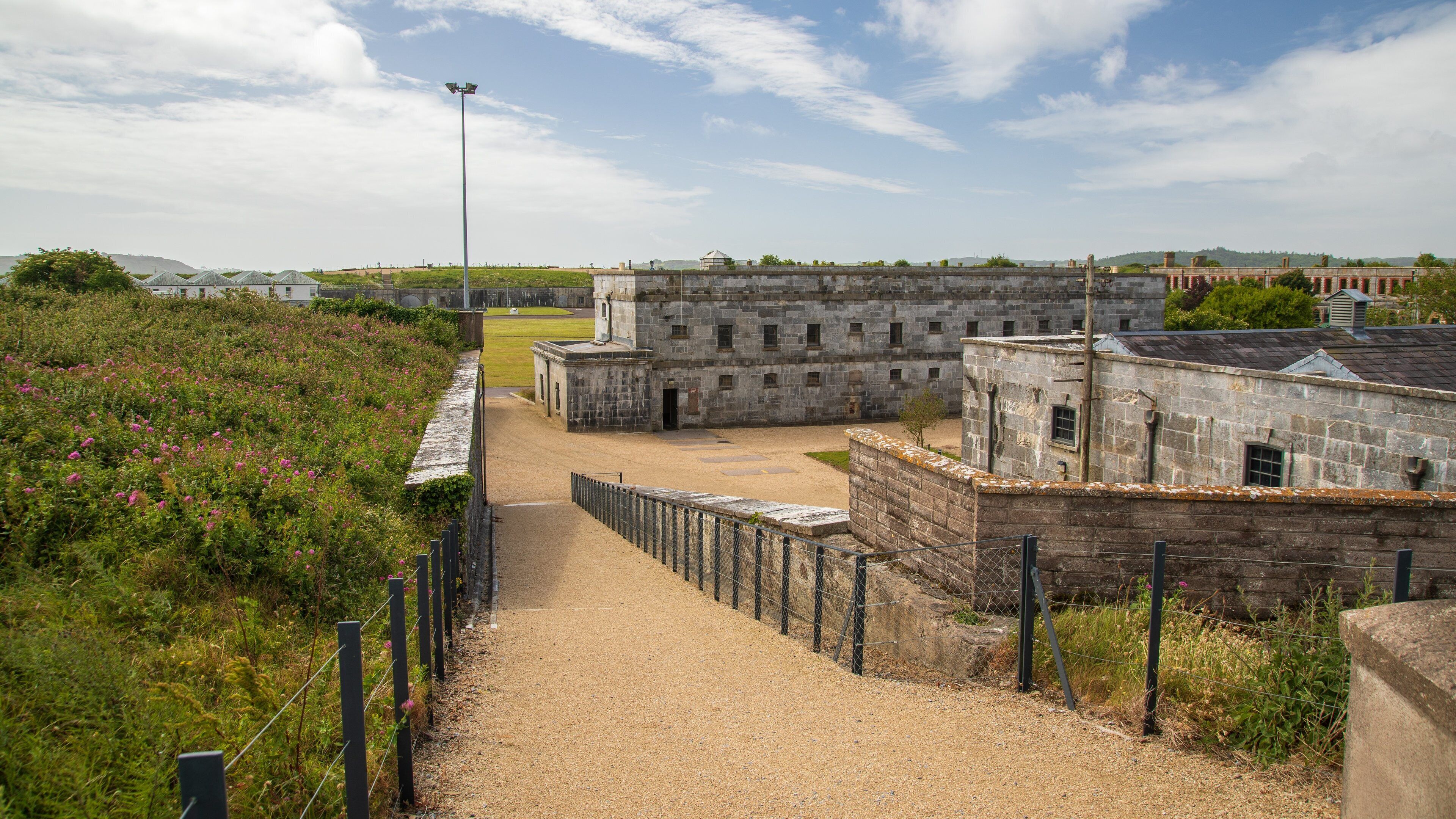 A historic stone building with a gravel path leading to it, surrounded by greenery and a clear sky.