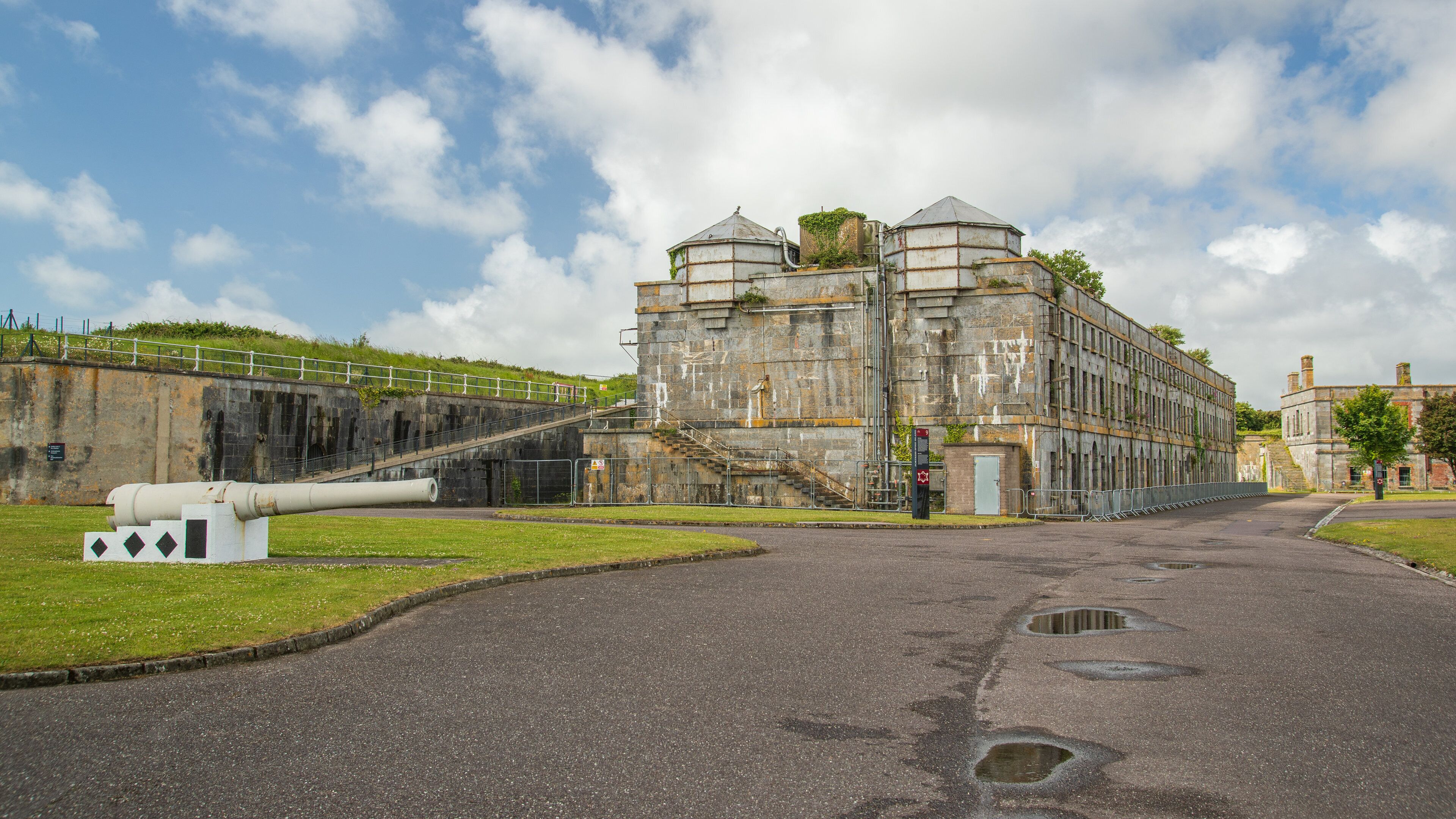 A historic building with a large cannon, a staircase leading to a turret, and a grassy area with a fence.