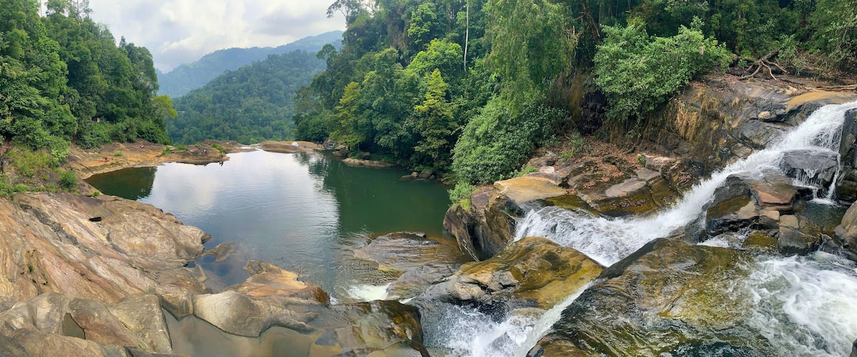 A waterfall cascading over rocks into a calm river surrounded by dense forest.