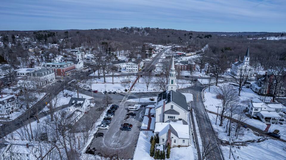 A snow-covered town with a prominent church steeple, a main road, and several residential buildings.