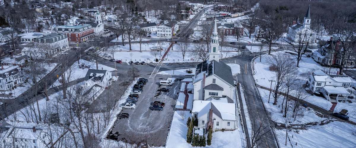 A snow-covered town with a prominent church steeple, a main road, and several residential buildings.