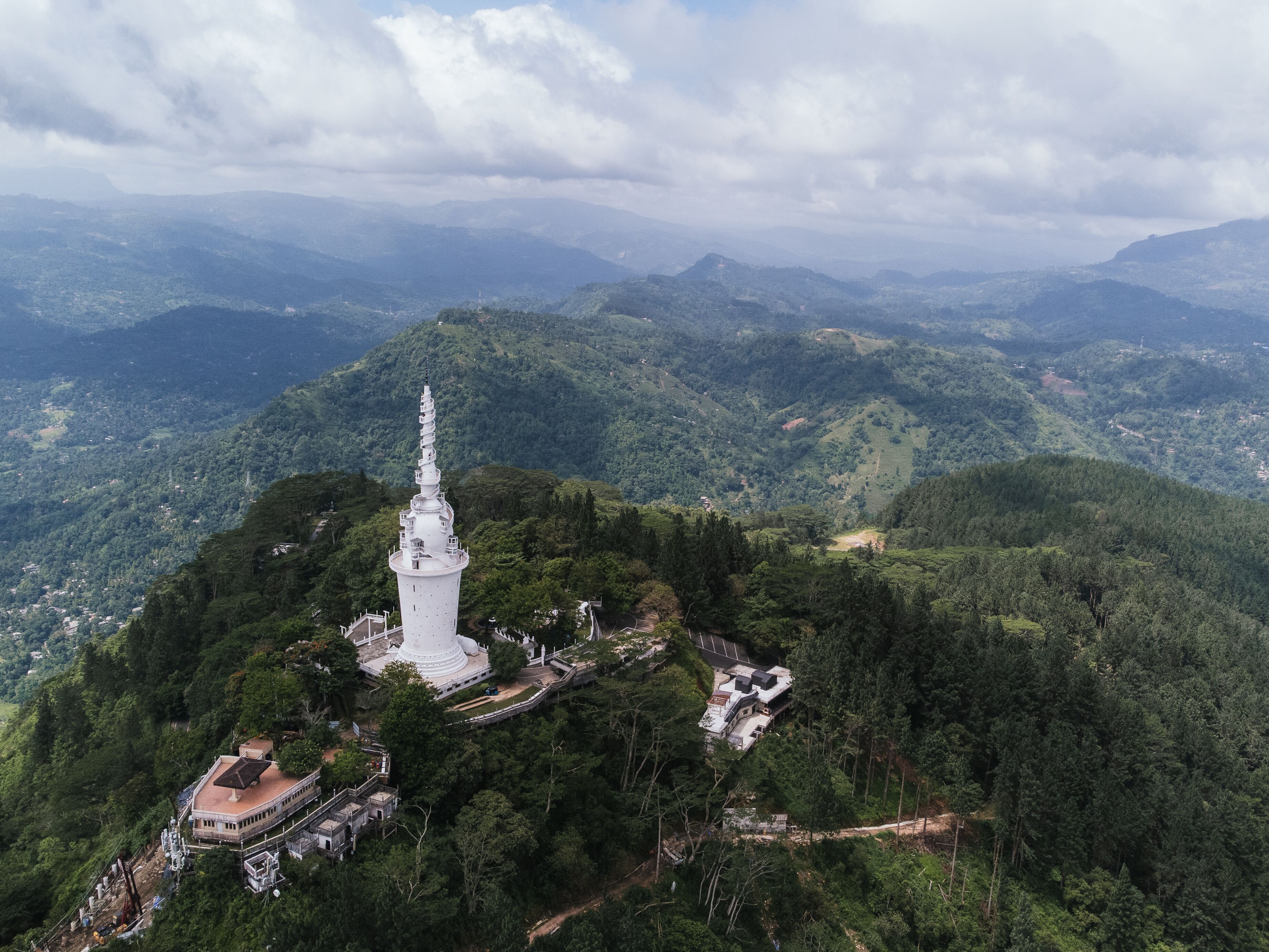 Aerial view of the white Ambuluwawa Tower located on a mountain peak surrounded by lush greenery, in Kandy, Sri Lanka
