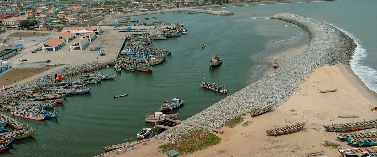 A coastal town with a marina filled with boats, a sandy beach, and a rocky shoreline.