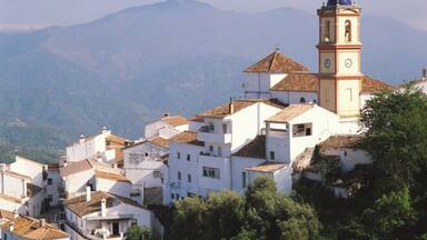 Un pueblo montañoso con edificios blancos y una imponente torre de iglesia con reloj.