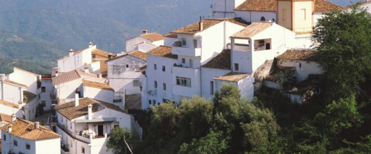 A mountainous village with white buildings and a prominent church tower with a clock.