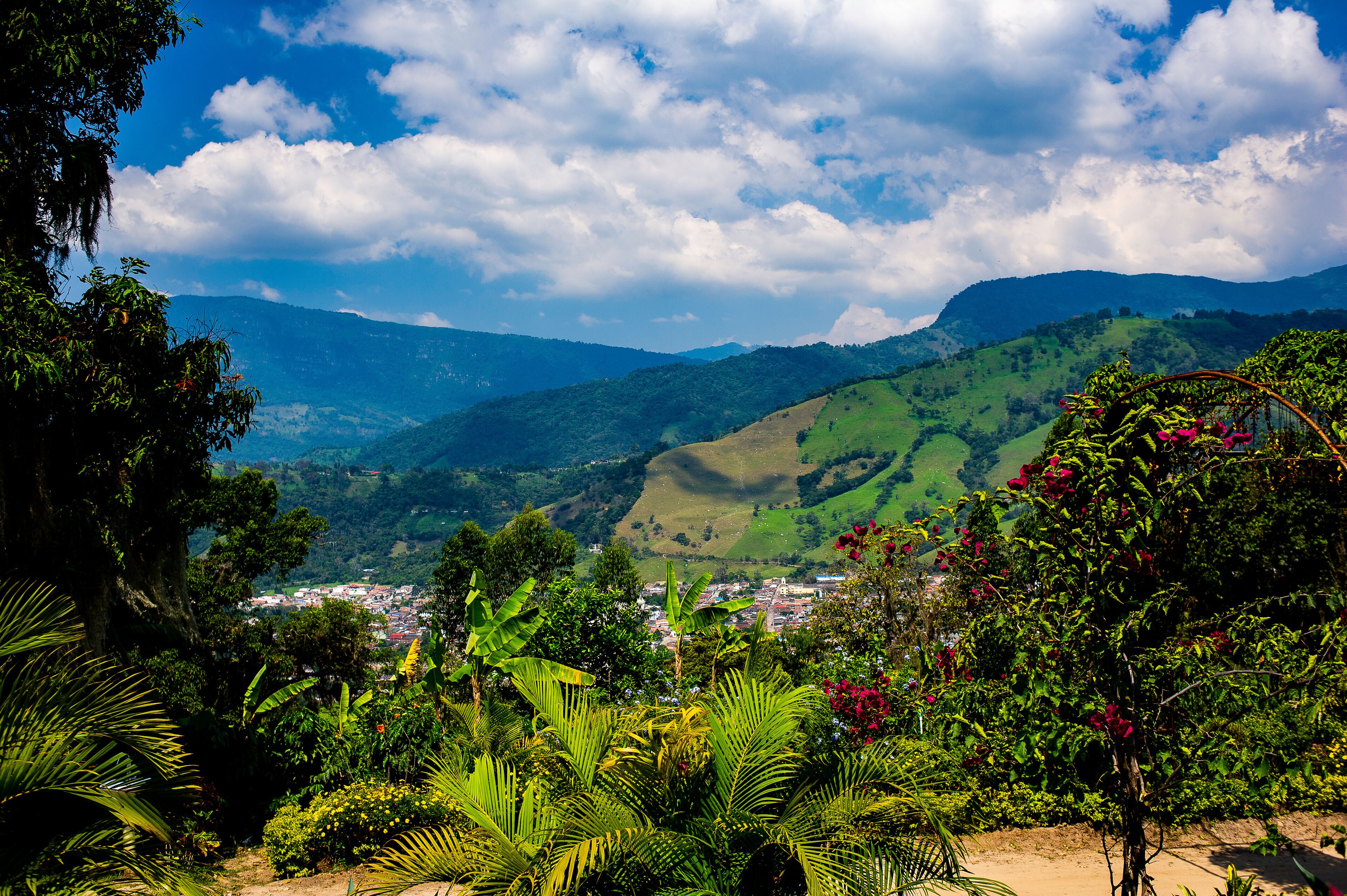 A lush green valley with a town nestled among hills, under a partly cloudy sky.
