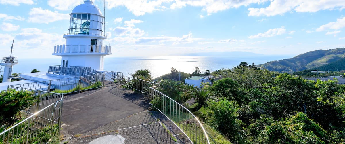 A lighthouse with a clear view of the sea and hills in the background.