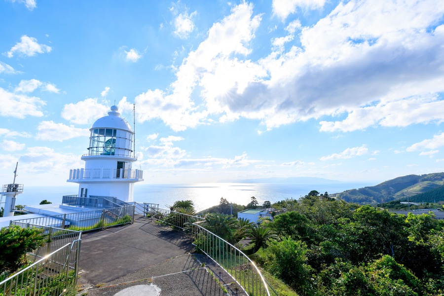 A lighthouse with a clear view of the sea and hills in the background.