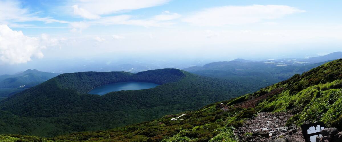 A mountainous landscape with a lake surrounded by lush greenery and a clear sky.