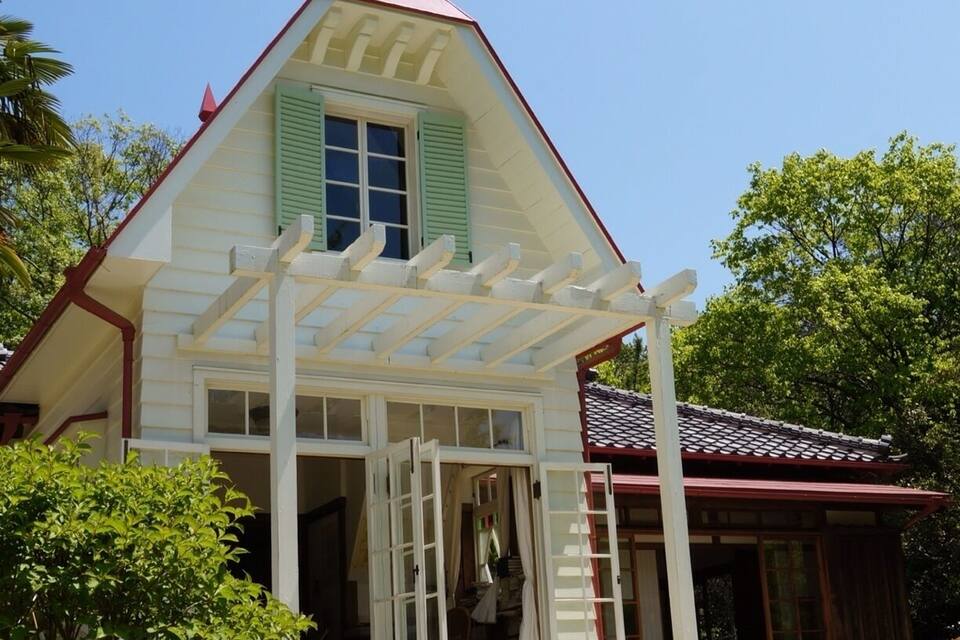 A quaint house with a red roof, green shutters, and a white porch.