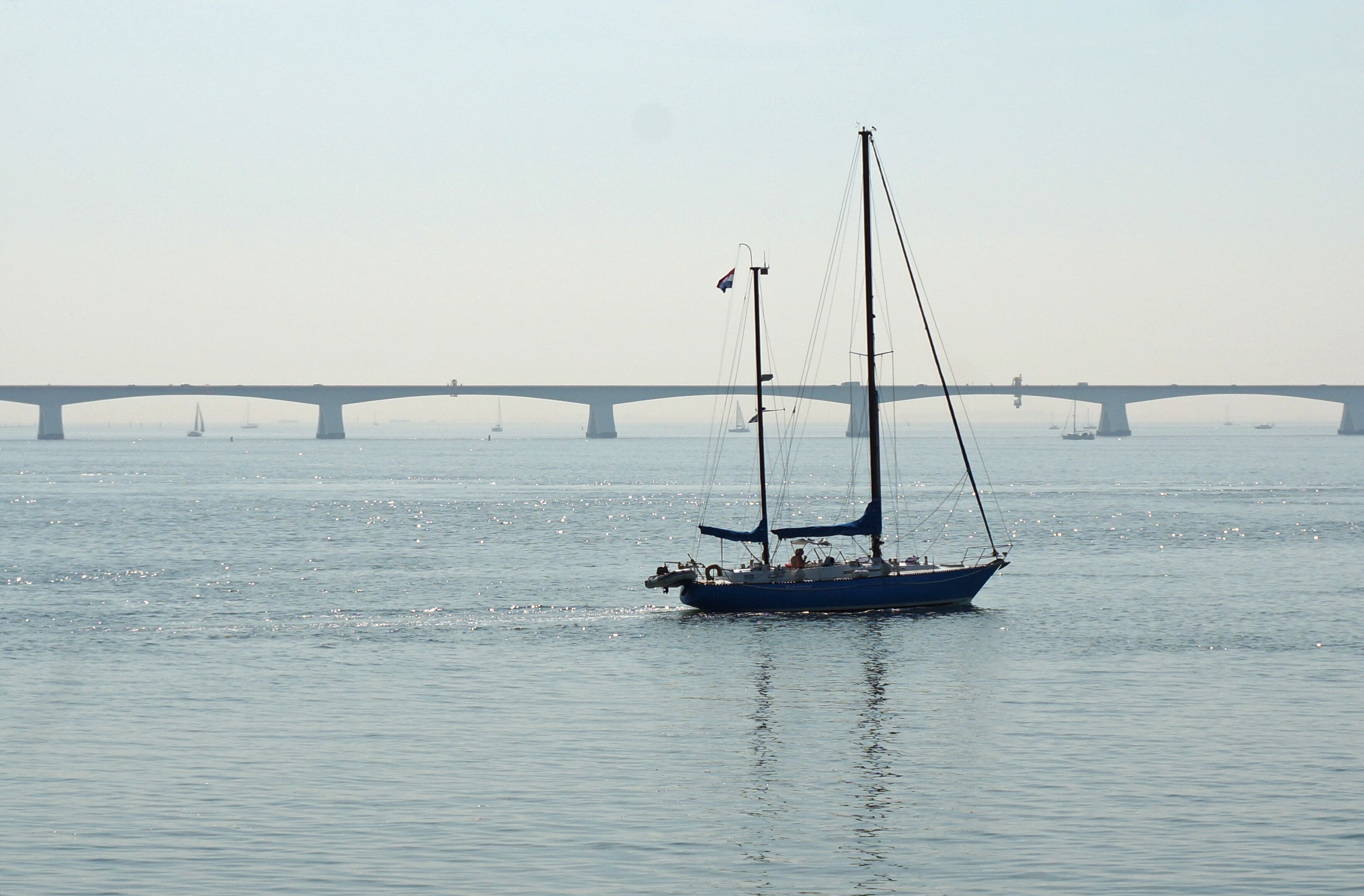 A sailboat on calm water with a bridge in the background.