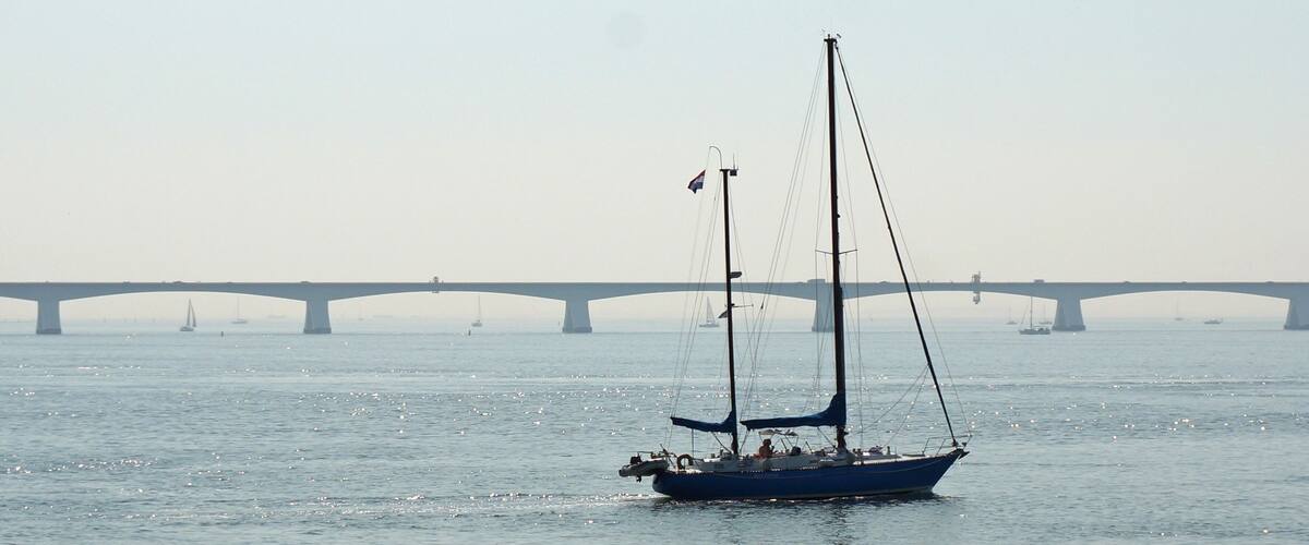 A sailboat on calm water with a bridge in the background.