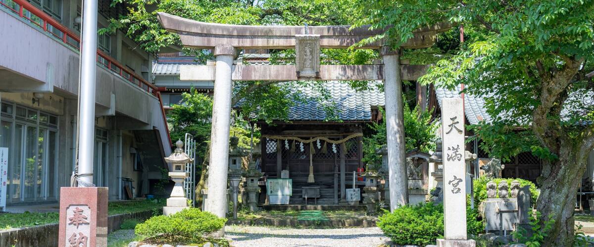 A traditional Japanese torii gate with a shrine in the background, surrounded by lush greenery and a stone monument with Japanese characters.
